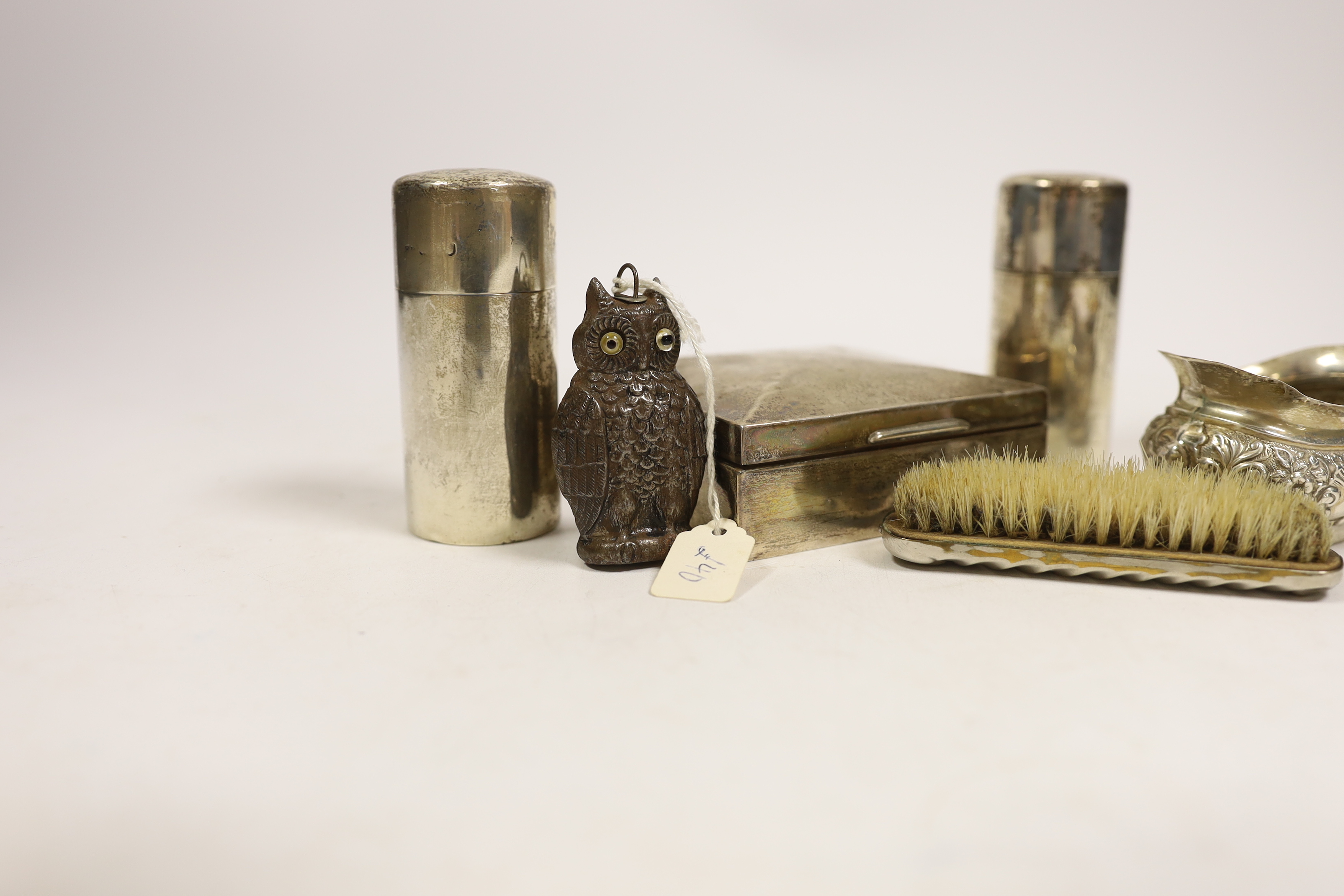 A late Victorian embossed silver cream jug, a pair of silver toilet bottles, a silver backed brush, a silver cigarette box and two other items.